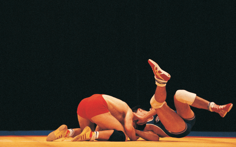 Wrestling competition with athletes in regulation gear, surrounded by official rules and equipment